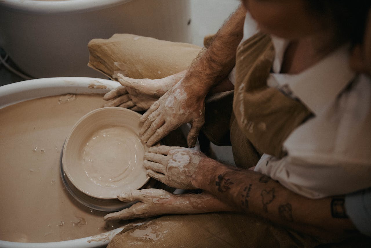 Artisan shaping clay on a pottery wheel with delicate hands, showcasing craftsmanship.