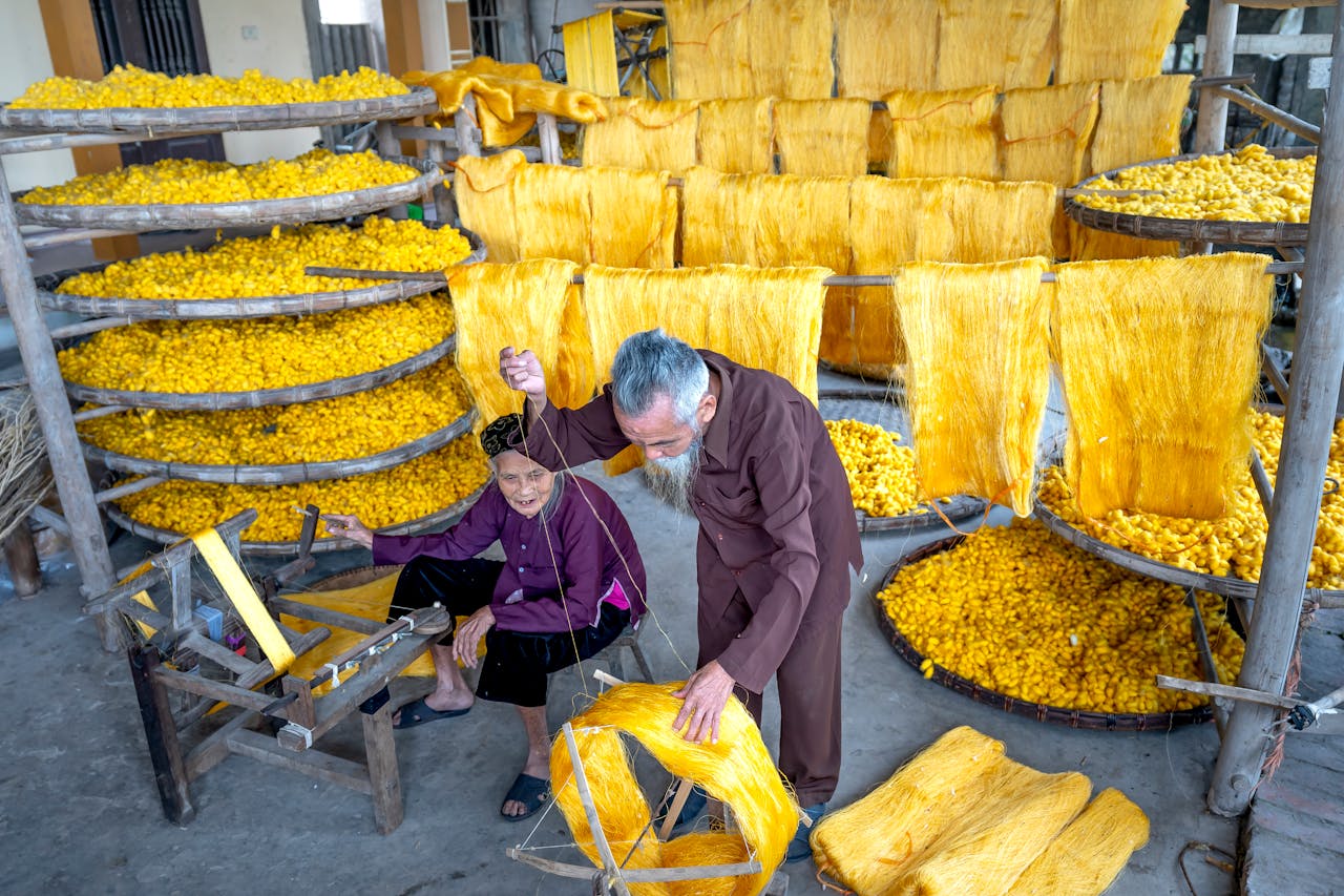 Elderly artisans work meticulously in a traditional textile workshop, processing yellow silk threads.